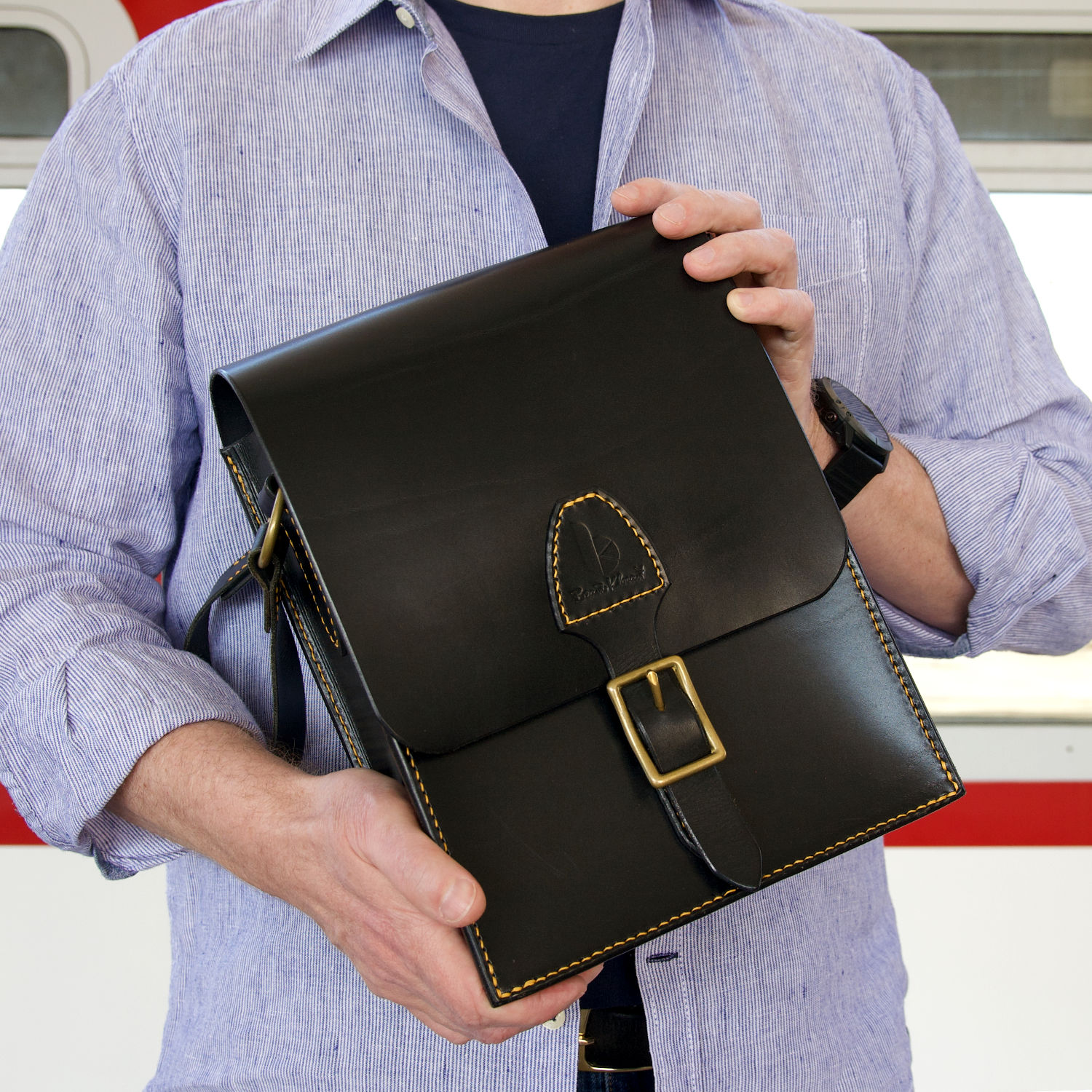 kožená messenger taška s mosadznou prackou držaná v rukách